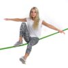 Junge Frau balanciert auf einer grünen Slackline, ideal für Anfänger und Fortgeschrittene, mit Fokus auf Gleichgewicht und Geschicklichkeit.