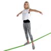 Junge Frau balanciert auf einer grünen Slackline mit sportlicher Kleidung und Konzentration, ideal für Fitness und Balance-Training.