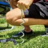 Mann kniet auf Rasen und hält spiralförmigen Erdanker aus verzinktem Stahl zur Befestigung von Outdoor-Ausrüstung, ideal für Trampoline, Zelte und Gartenmöbel.