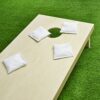 Set mit weißen Cornhole Wurfsäckchen auf einem Spielbrett in einem grünen Garten, bereit für ein geselliges Spiel.