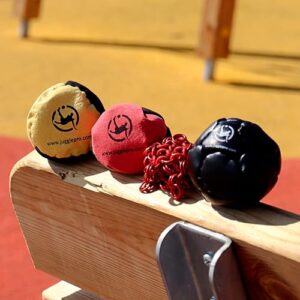 Juggle Pro Footbag Adventure auf einer Holzoberfläche, umgeben von bunten Jonglierbällen und einem Kettenglied, geeignet für Freestyle-Jonglage und Outdoor-Aktivitäten.