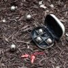 Kikkerland GG90 Boules Set S mit silbernen Kugeln in einem offenen schwarzen Etui auf Holzschnitzelboden, ideal für Boule- und Boccia-Spiele im Freien.