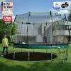KINETIC SPORTS Trampolin im Federlos-Design 'Bungee Safety Elite' im Garten mit Sicherheitsnetz, geeignet für Kinder und Erwachsene. Der Junge in grüner Jacke plant, auf dem Trampolin zu springen, während ein Fußball darauf liegt. Modernes Umfeld mit gepflegtem Garten.