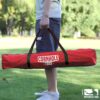 Person hält eine robuste rote Tragetasche mit dem Aufdruck 'CORNHOLE TOSS' in einer sonnigen Outdoor-Umgebung, ideal für Freizeitaktivitäten und Spiele im Freien.