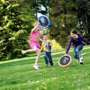 Kinder spielen im Freien mit dem Schildkröt® Ogo Sport Set, bestehend aus zwei Ogo Softdiscs und einem Wuschelball, in einem sonnigen Park.